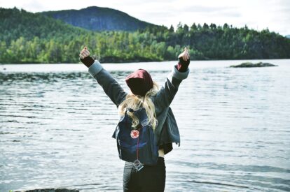 Person standing at a lake with hands up.