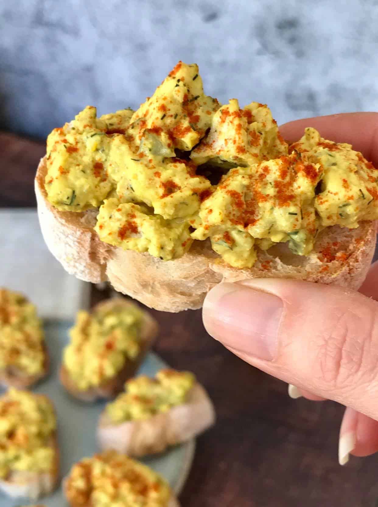 Hand holding a piece of vegan deviled egg crostini.