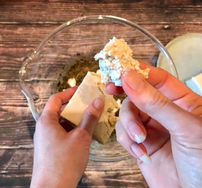 Hand breaking tofu into chunks.