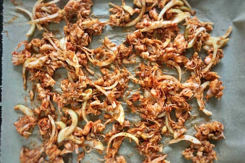 Vegan jackfruit pulled pork on sheet tray with onions and BBQ sauce.