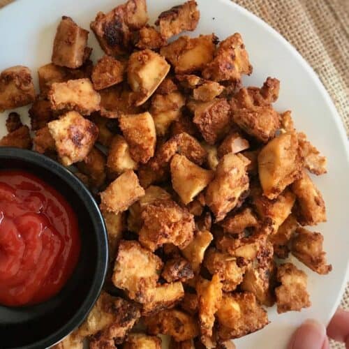 Tofu nuggets on a plate with a small bowl of ketchup.