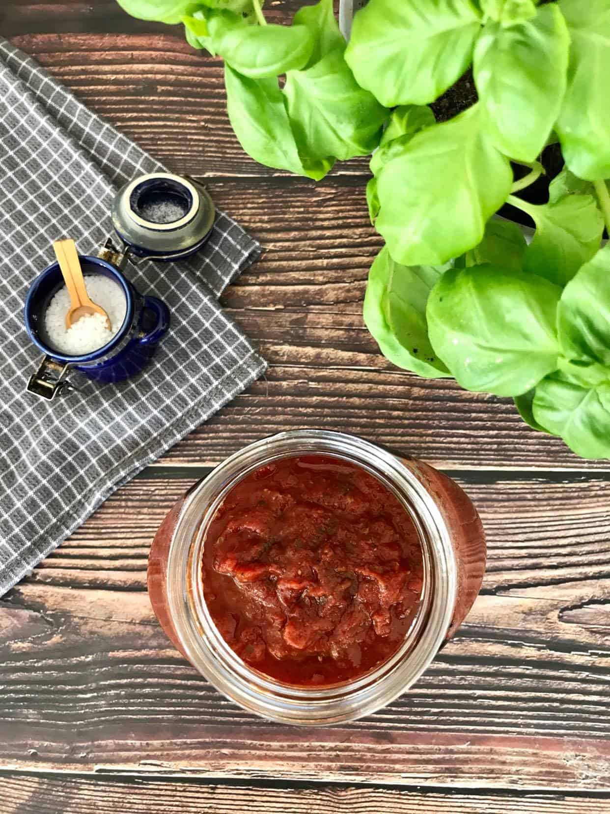 Vegan tomato sauce in jar with salt and basil leaves.
