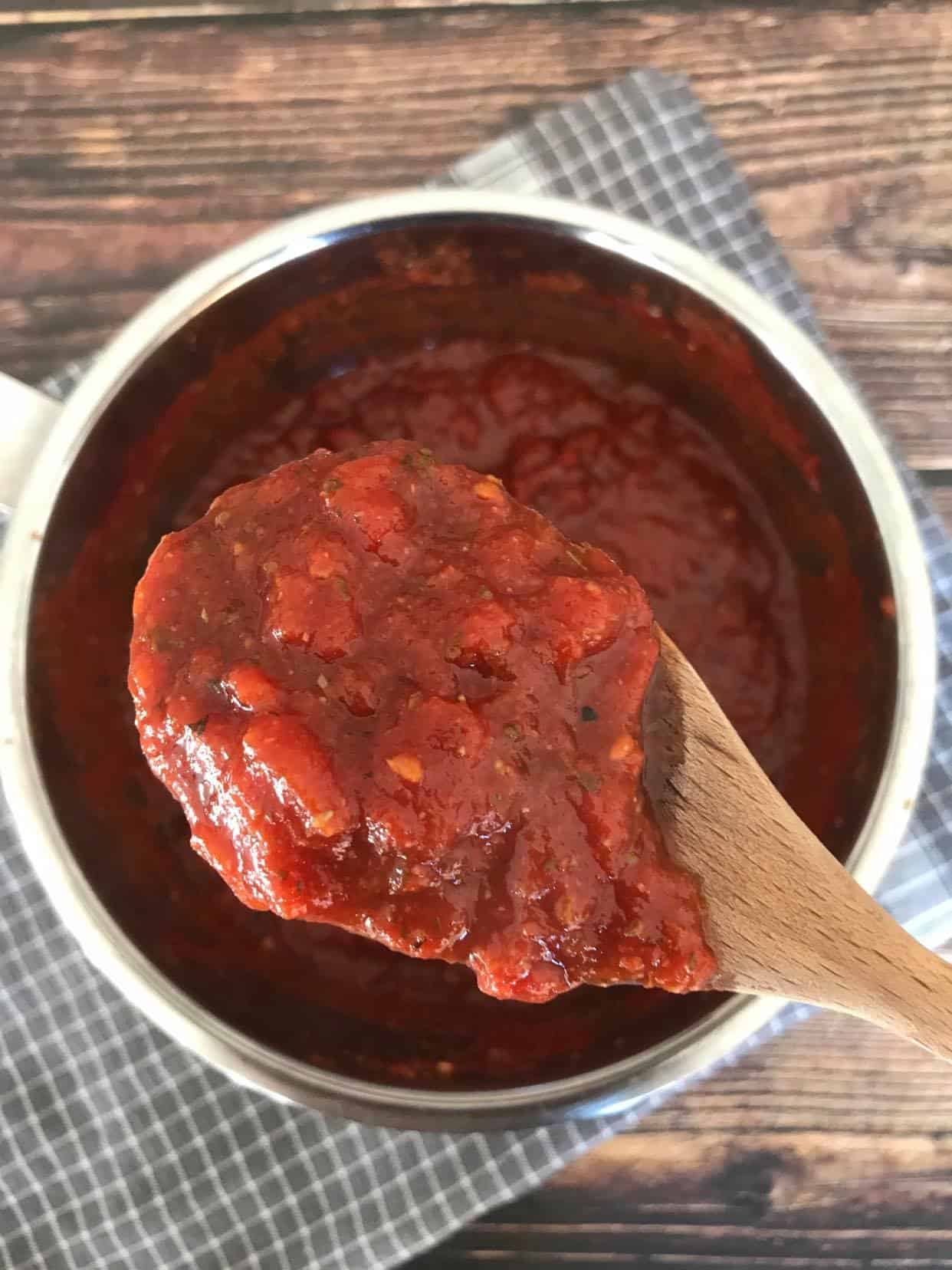 Hearty marinara sauce in pot with spoon lifting up.