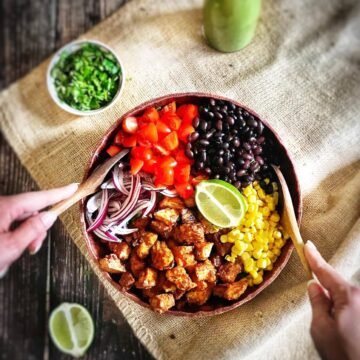 Southwestern salad with chili-lime tofu nuggets in a bowl with two hands tossing it.