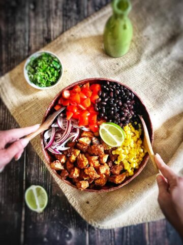 Southwestern salad with chili-lime tofu nuggets in a bowl with two hands tossing it.