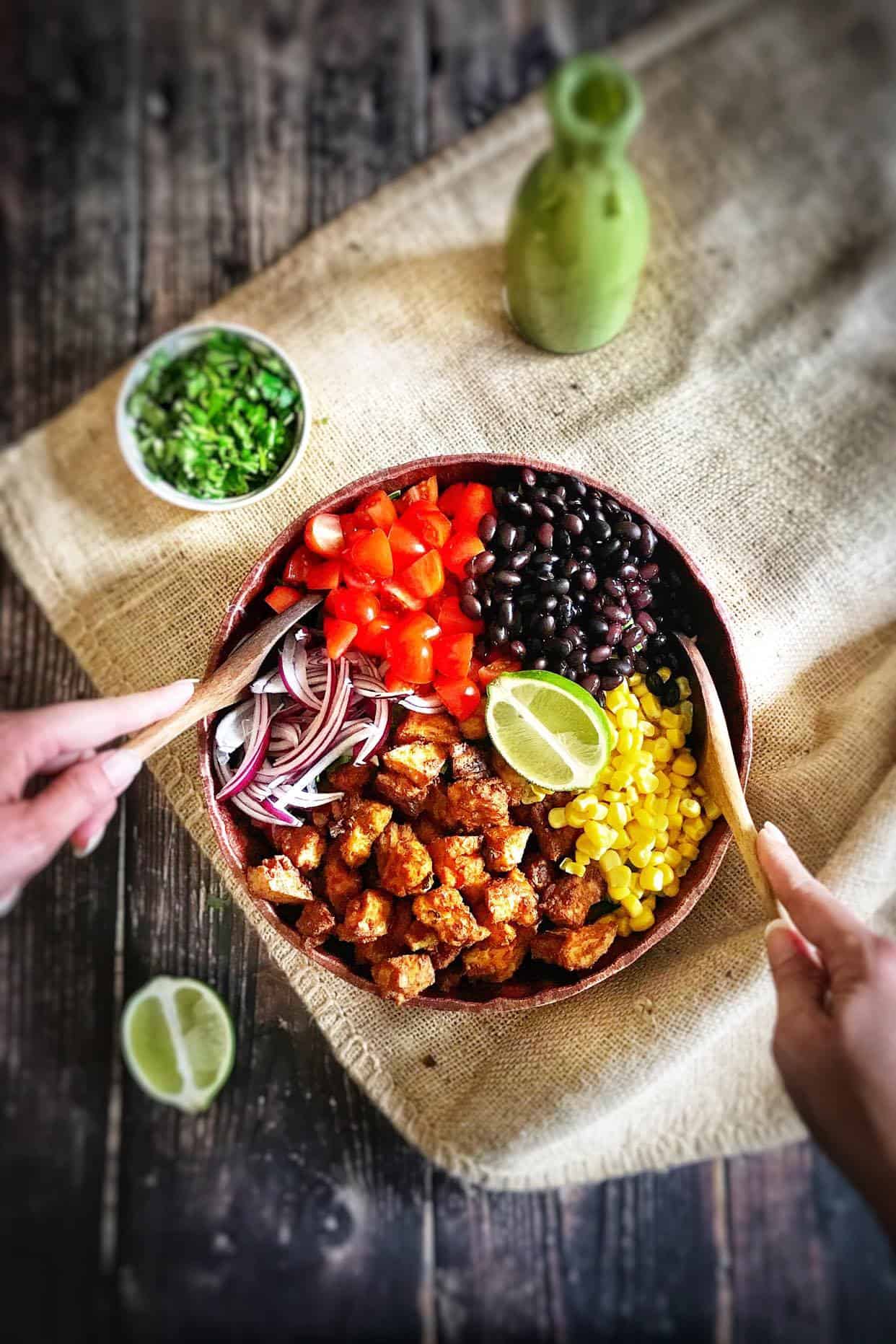 Southwestern salad with chili-lime tofu nuggets in a bowl with two hands tossing it.