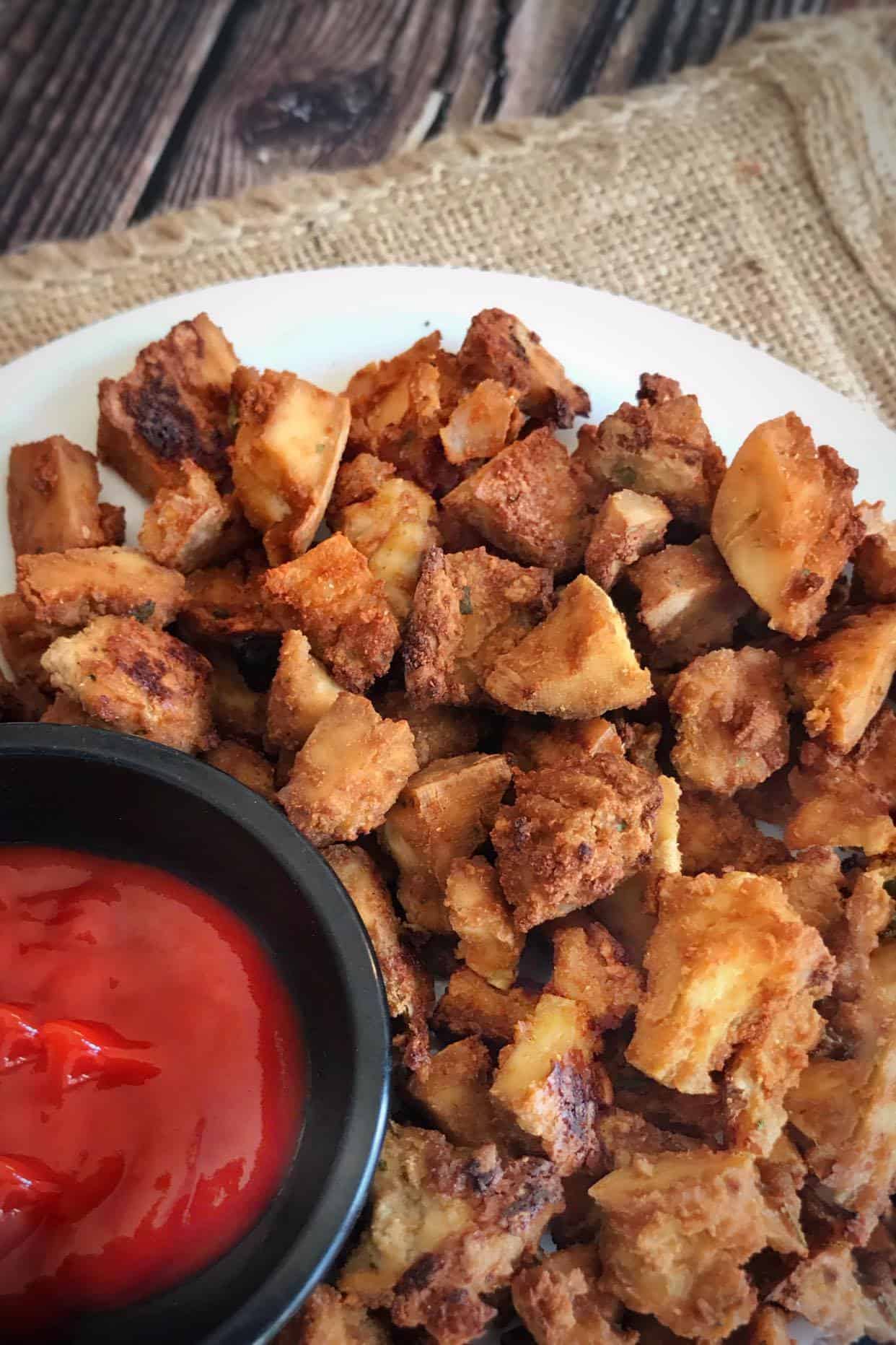 Tofu nuggets on a plate with a small bowl of ketchup.