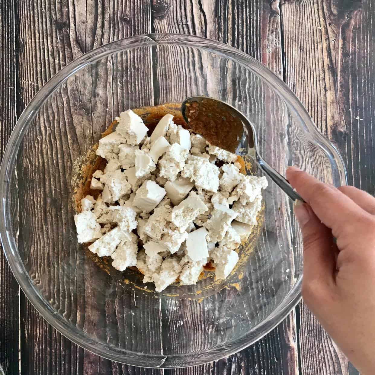 Tofu nuggets in a bowl with a hand about to mix them into the paste.