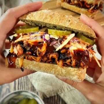 Hands holding a vegan BBQ jackfruit sandwich.