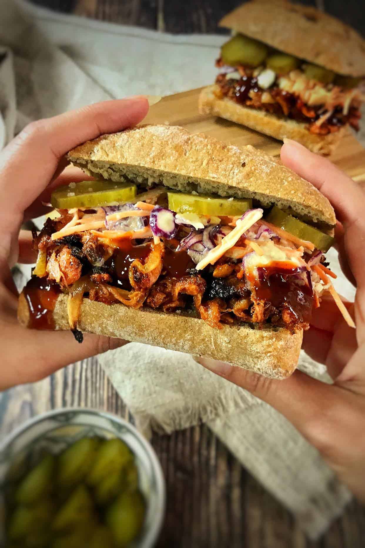 Hands holding a vegan BBQ jackfruit sandwich.