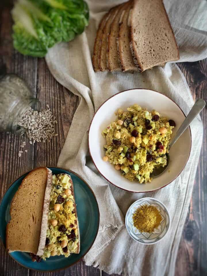 Vegan curry chickpea salad in a bowl next to a sandwich and other ingredients.