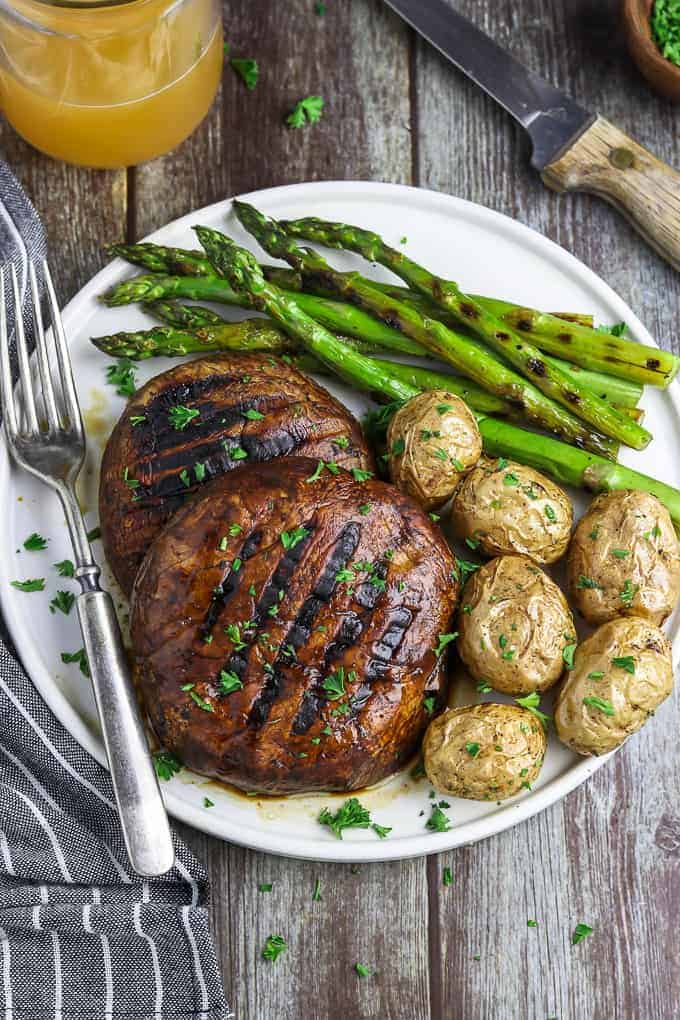 Grilled portobello mushroom steaks on a plate with potatoes and asparagus.