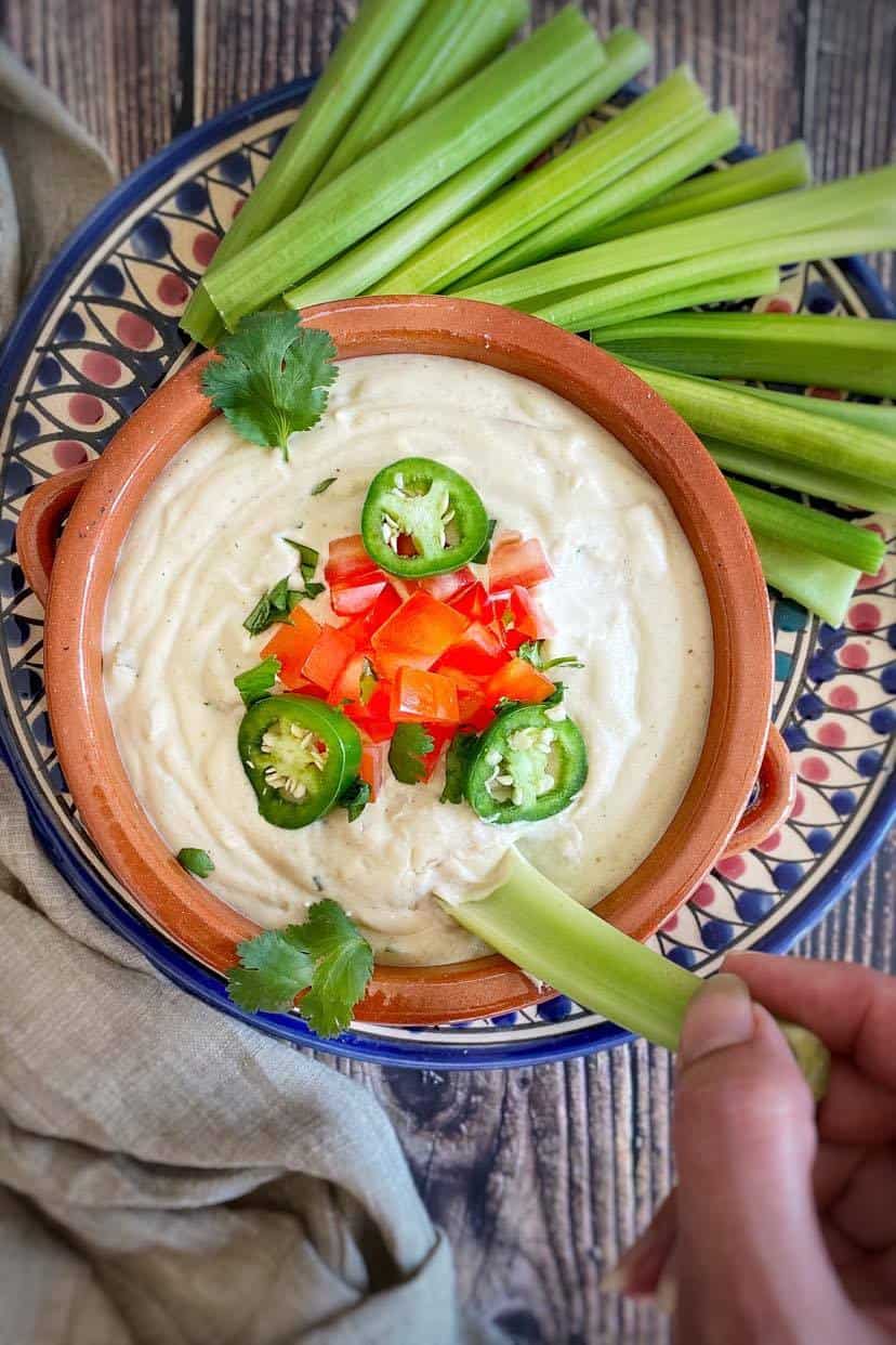 Hand dipping celery into cashew queso.