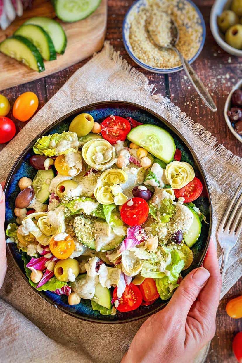 Hands holding a bowl of vegan Italian salad.