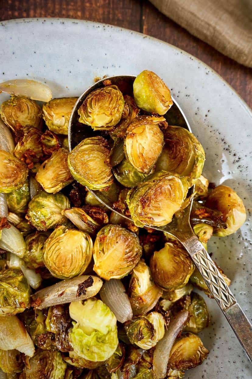 Spoon lifting maple balsamic roasted Brussels sprouts from a bowl.