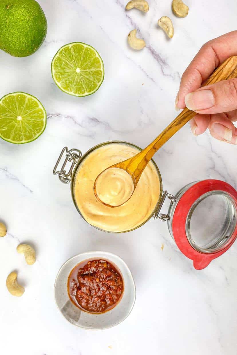 Hand lifting a spoonful of chipotle mayo from a jar.