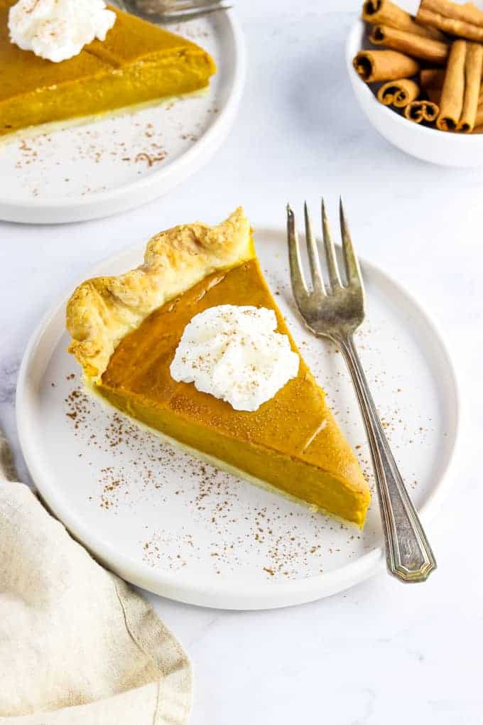 Vegan pumpkin pie on a plate with whipped cream and a fork.