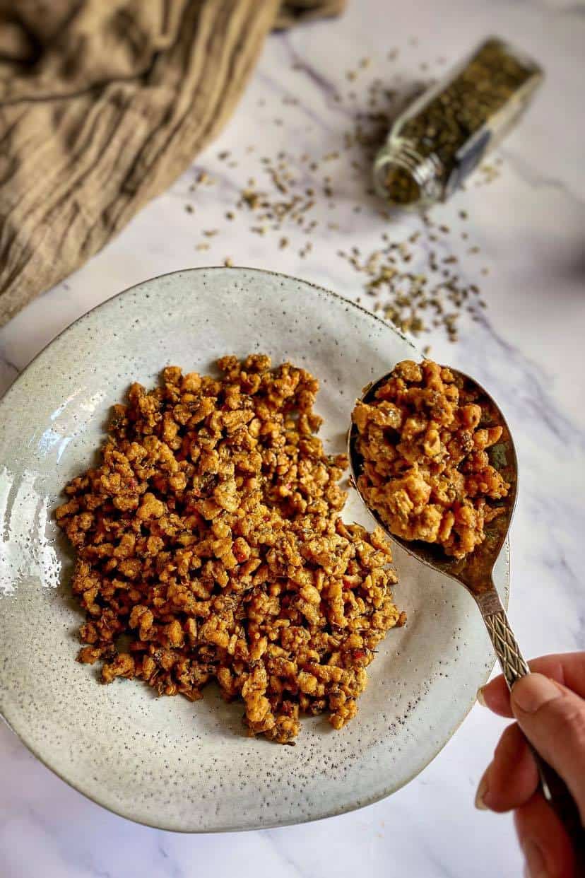 Hand lifting a spoonful of Vegan Italian sausage crumbles.