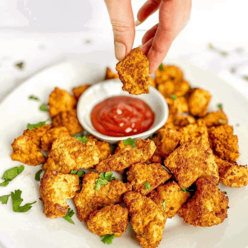 Hand dipping air fryer tofu nugget into ketchup.