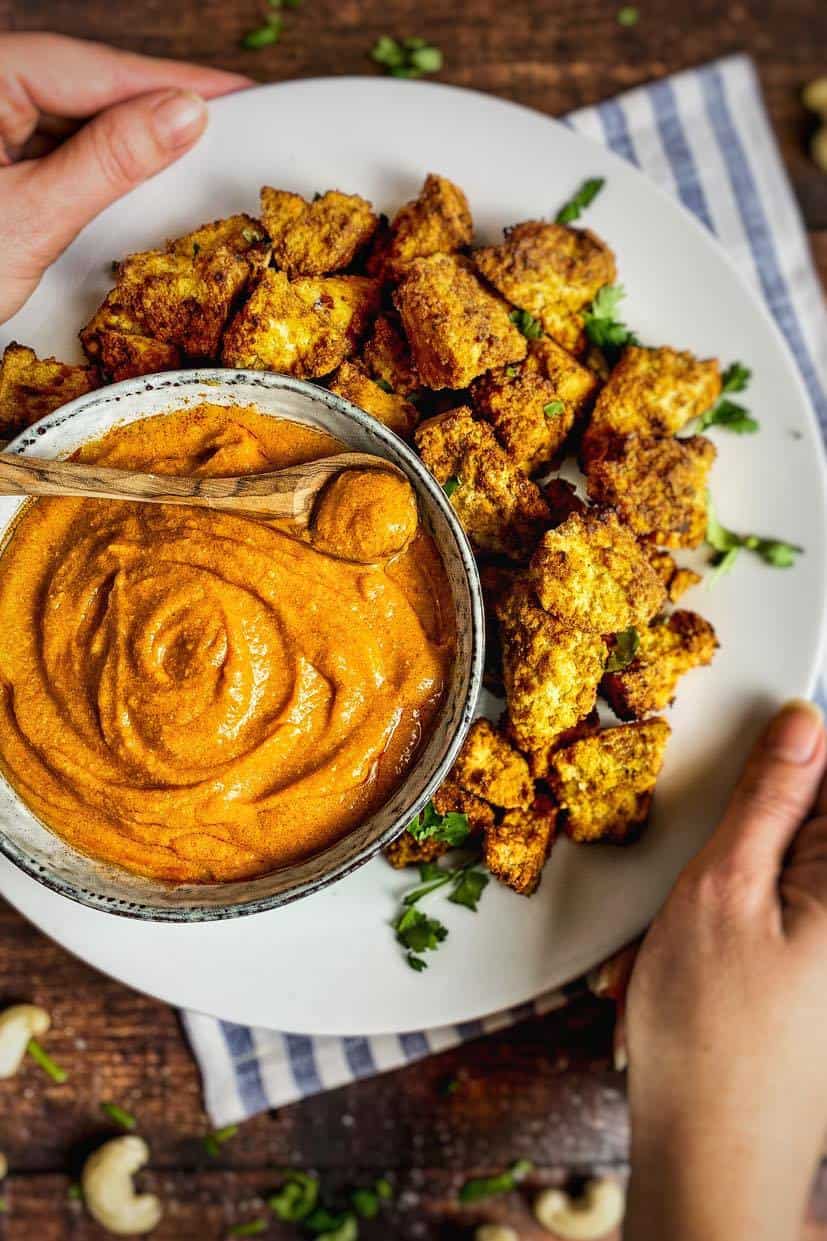 Vegan buffalo sauce in a bowl surrounded by tofu nuggets.