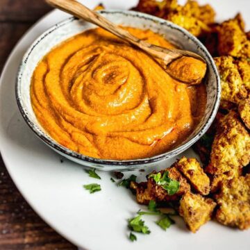 Vegan buffalo sauce in a bowl surrounded by tofu nuggets.