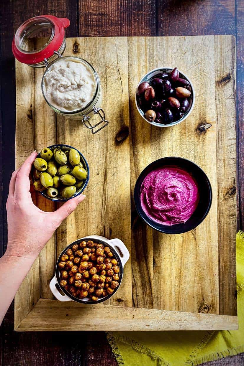 Hand arranging bowls on a vegan charcuterie board.