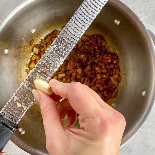 Hand grating garlic over a pot.