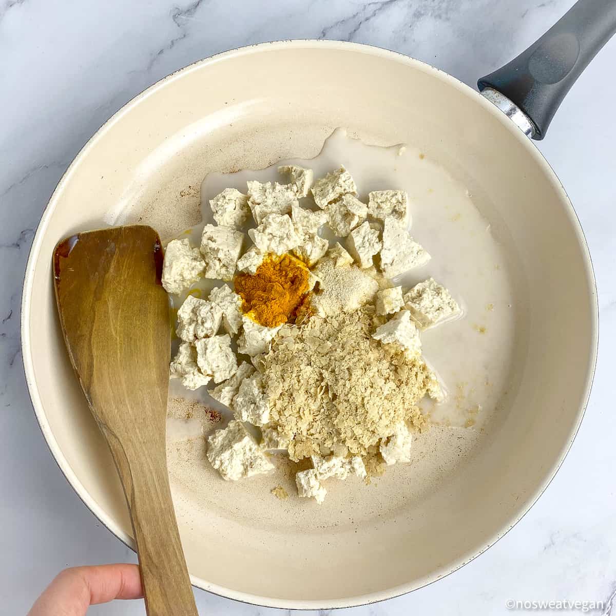 Add nutritional yeast, turmeric, garlic, onion powder, and soy milk to the tofu scramble.