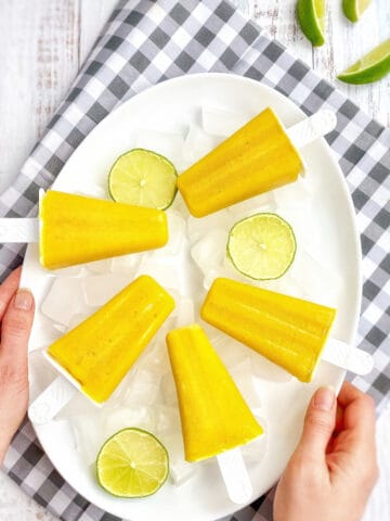 Mango popsicles on a plate with limes.