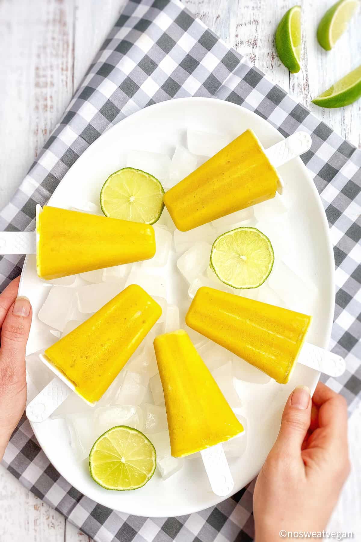 Mango popsicles on a plate with limes.