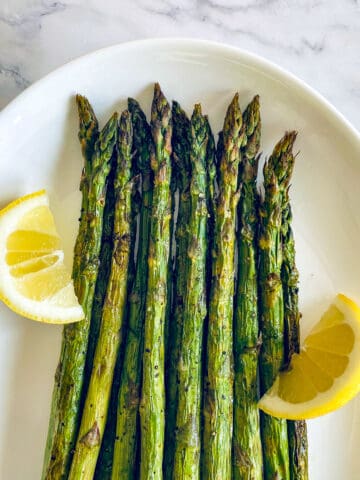 Air fryer asparagus on a plate with lemon wedges.