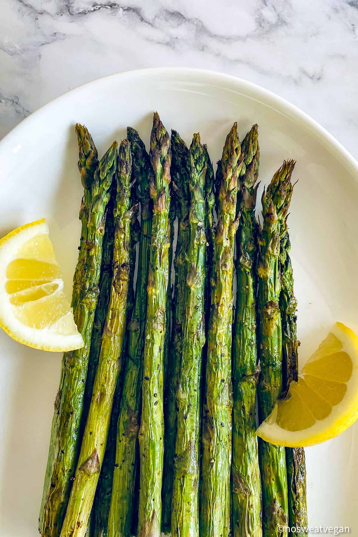 Air fryer asparagus on a plate with lemon wedges.