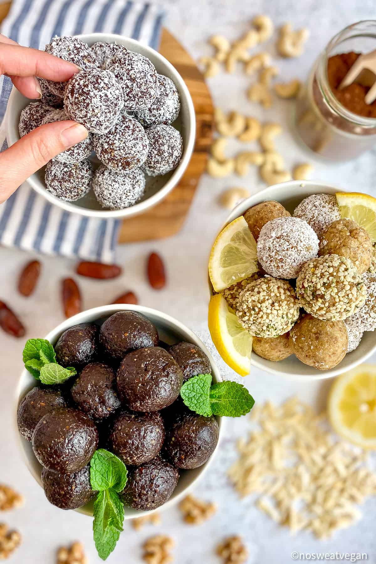 Vegan bliss balls in three bowls with a hand picking up one.