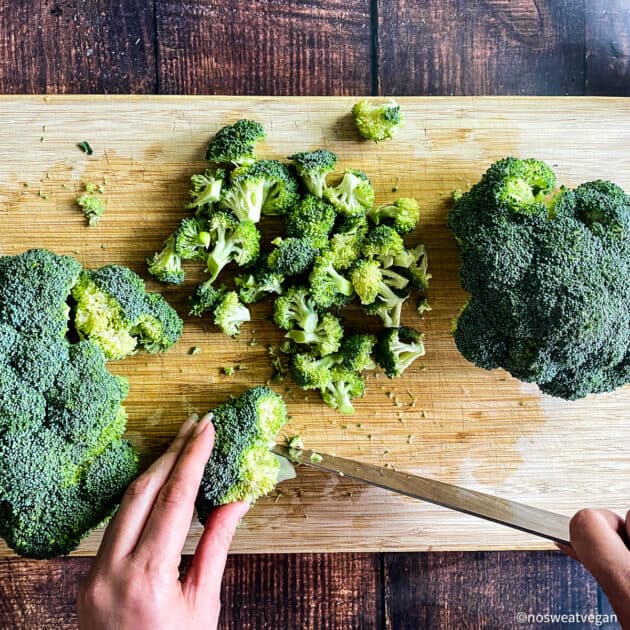Hand chopping broccoli on cutting board.