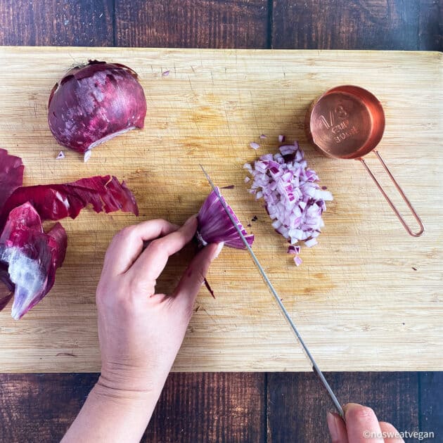 Hand dicing red onion on cutting board.