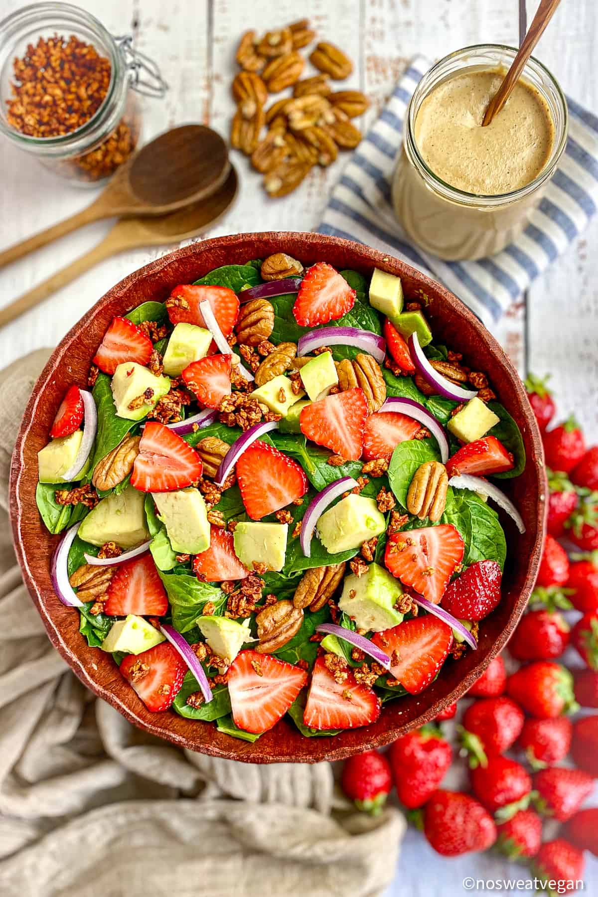 Bowl of spinach salad with strawberries, avocado, pecans, and vegan bacon bits. 