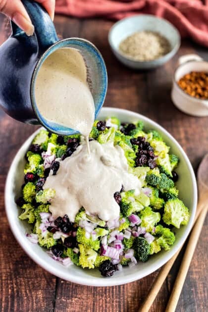 Hand pouring cashew dressing on the broccoli salad.
