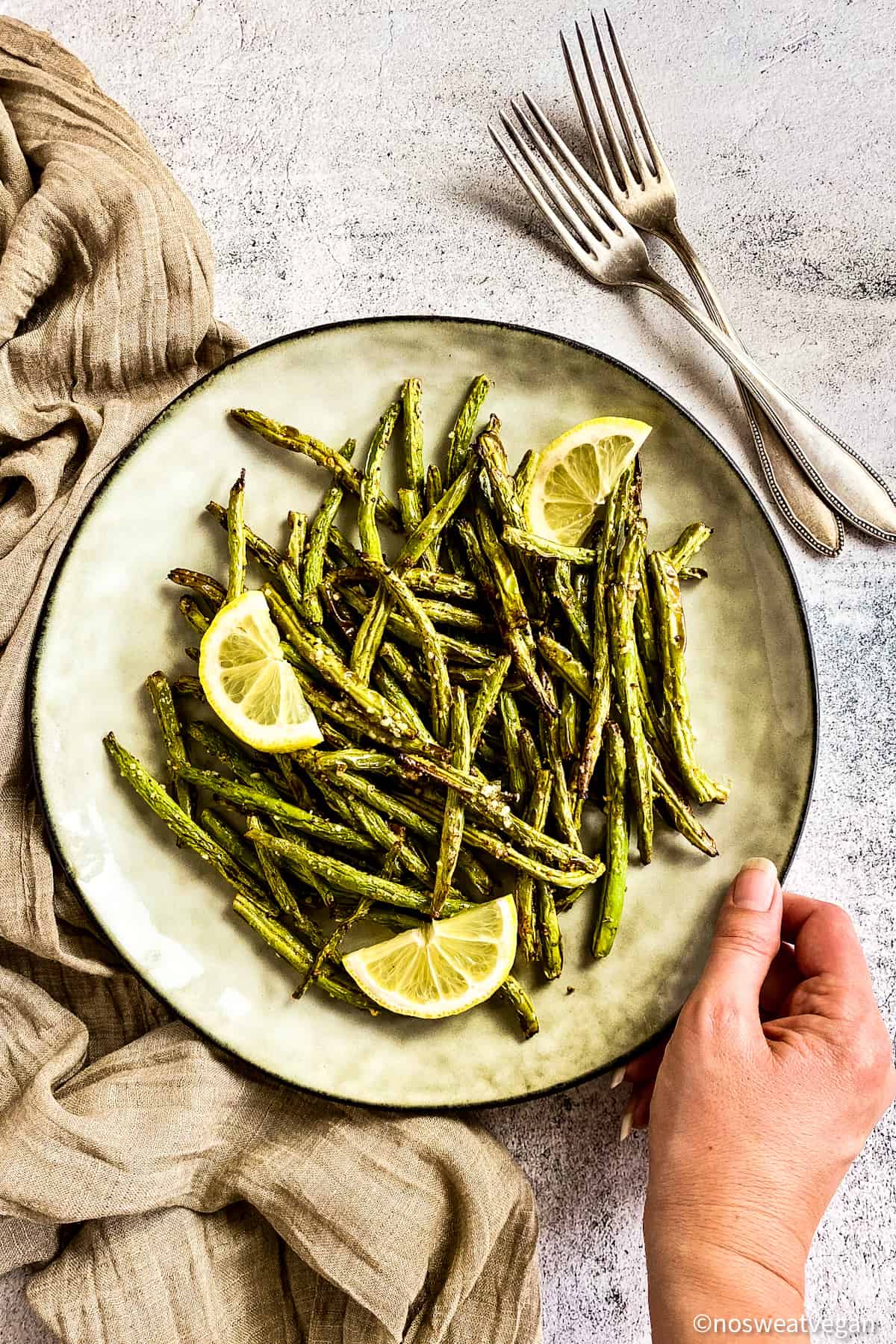 Air fryer green beans on plate with lemon wedges.