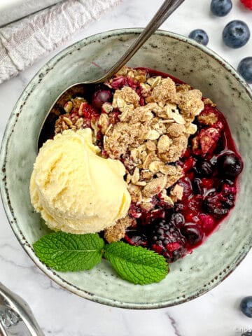 Vegan berry crumble in bowl with ice cream.