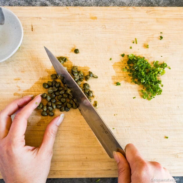 Hands chopping capers and parsley.