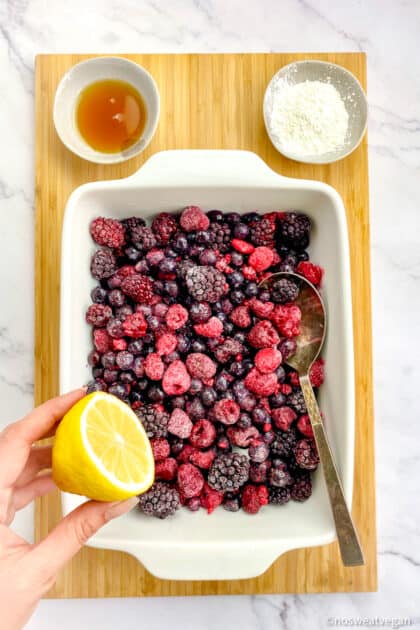 Frozen mixed berries in dish with hand squeezing lemon over the top.