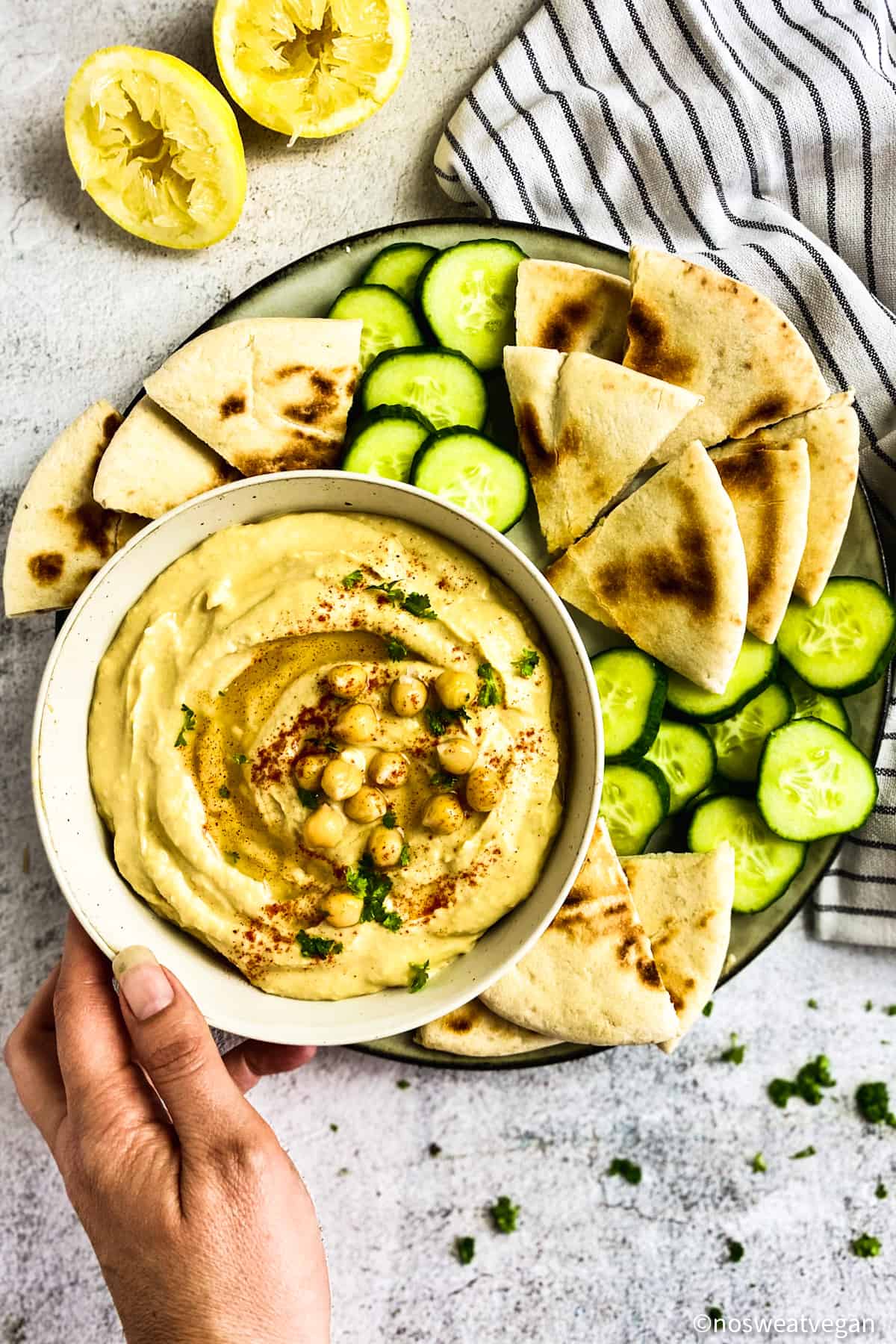 Hummus made without oil on a place with pita triangles and cucumbers.