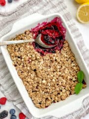 Vegan berry crisp in a baking dish with a spoon.