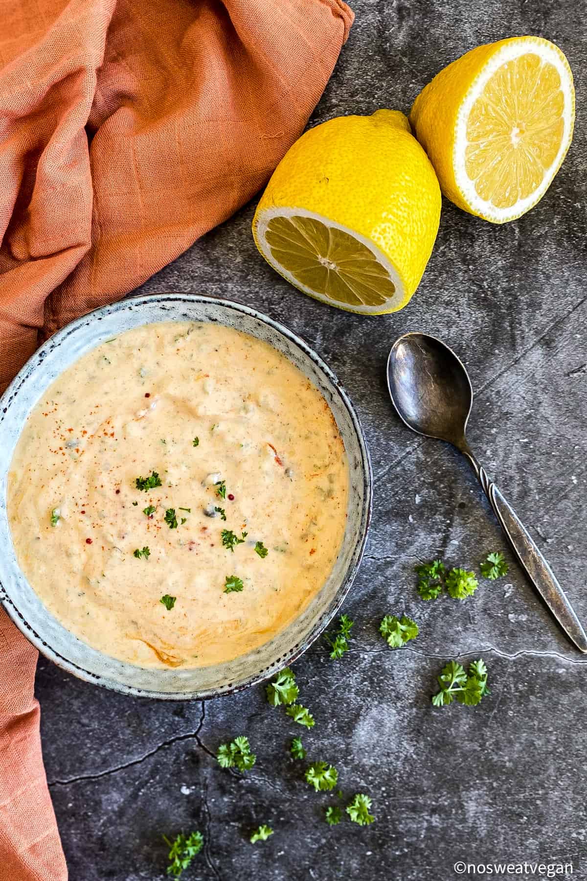 Vegan remoulade sauce in bowl with lemon, parsley, and a spoon.