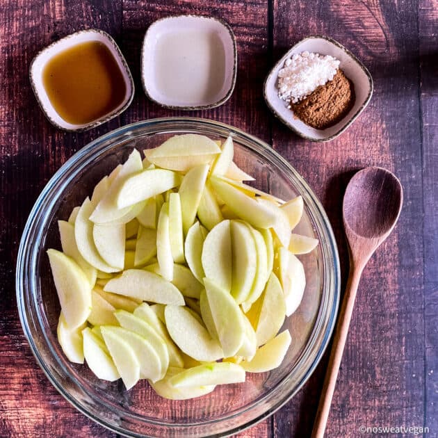 Apple slices in large bowl surrounded by smaller bowls with seasonings.