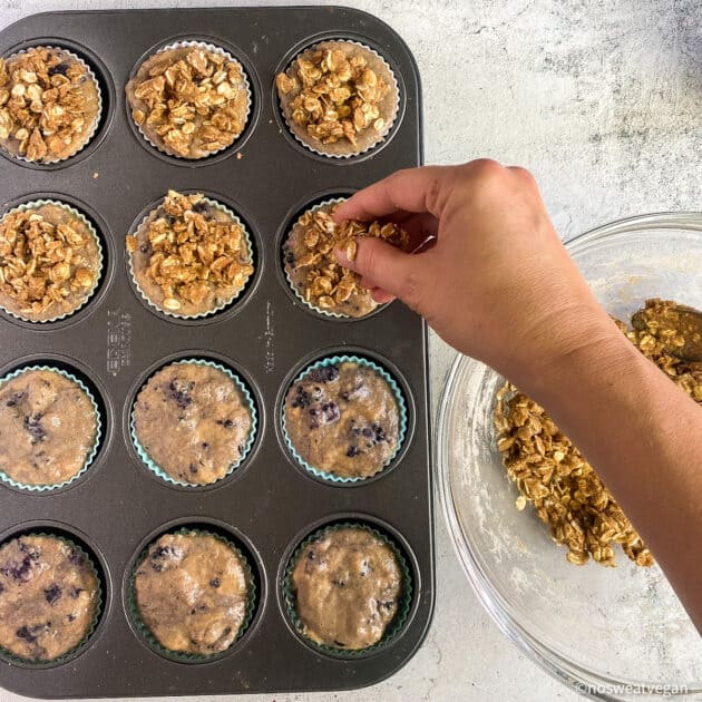 Hand adding streusel topping to muffins in tin.