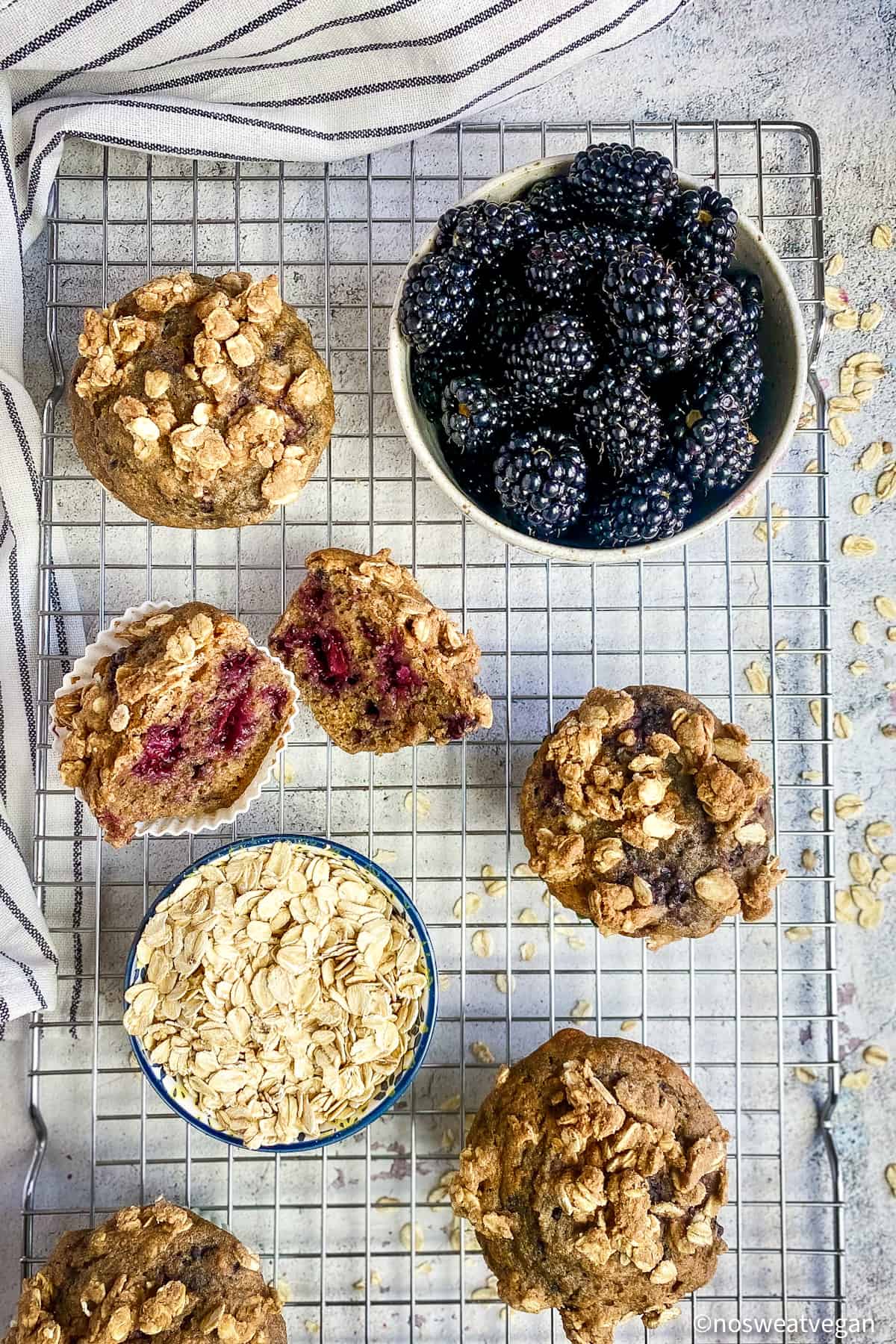 Oil-free blackberry muffins on drying rack with a bowl of blackberries and a bowl of oats.