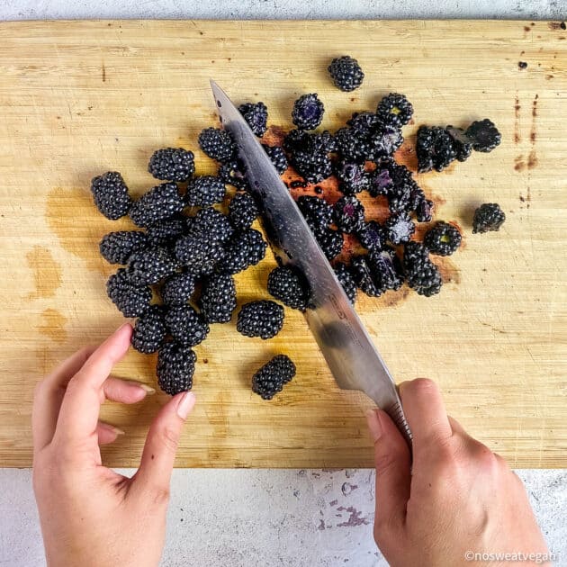 Hands chopping blackberries on a cutting board.