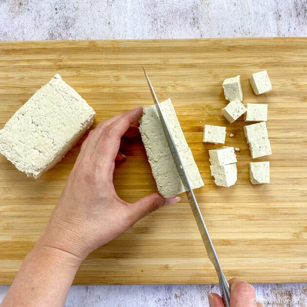 Hands cubing tofu on cutting board.