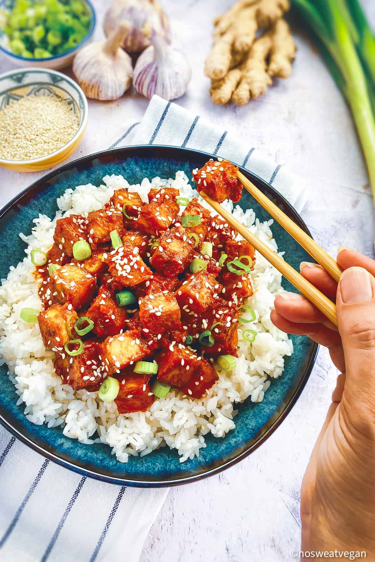 Hand with chopsticks picking up spicy Korean tofu.